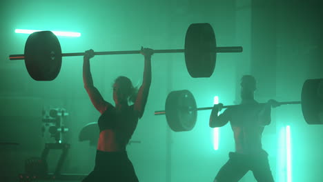 un hombre y una mujer en una luz de neón de colores rojo y azul en cámara lenta levantan pesadas barras sobre sus cabezas. entrenamiento de fuerza y potencia con pesas pesadas. el concepto de parejas atléticas y fuertes