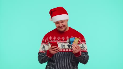 Mann-Im-Weihnachtspullover-Benutzt-Kreditkarte-Und-Smartphone,-Während-Er-Geld-Beim-Online-Einkauf-überweist