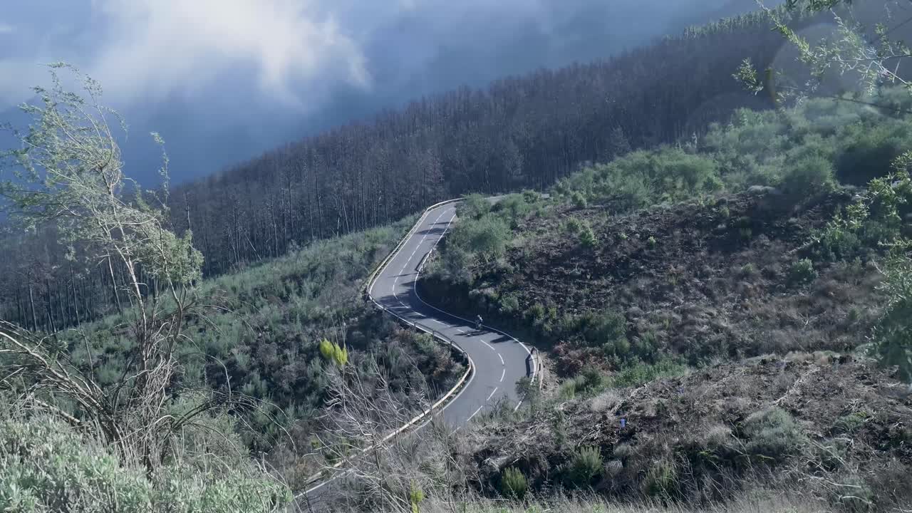 Mobil dan Sepeda Motor Berkendara di Jalan Gunung yang Berkelok Melintasi Lanskap Berawan