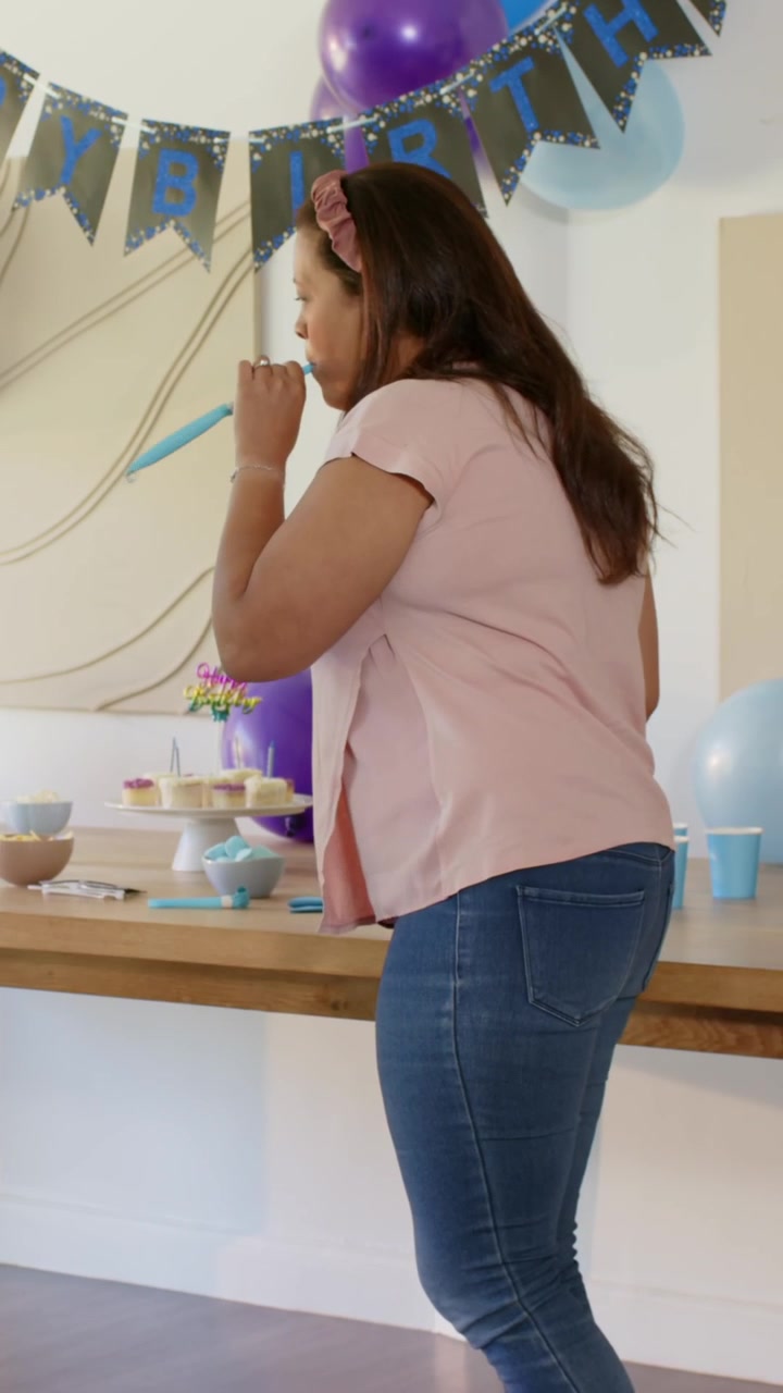 Donna trentenne che entra, sistema i pirottini dei cupcake, riempie una brocca, usa un gonfiatore e prepara la tavola di compleanno a casa.