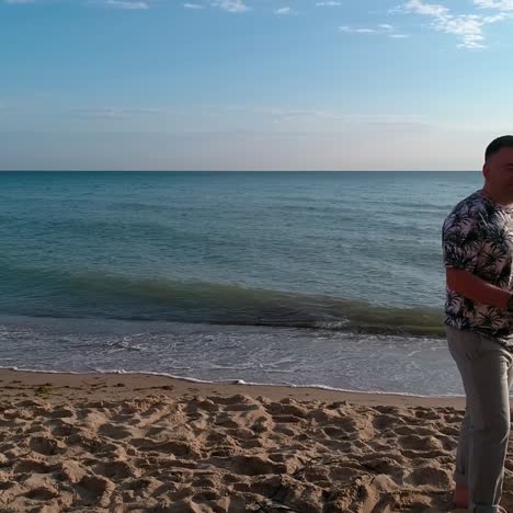 Man singer on a sea beach. Musician man singing into microphone while standing on a sand shore on blue sea background. Orbital view