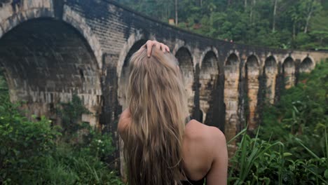 a young woman observes the historic nine arch bridge from a nearby hillside in ella, sri lanka.