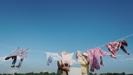 la niña ayuda a su abuela a colgar la ropa para secarla en un día claro de verano contra un cielo azul