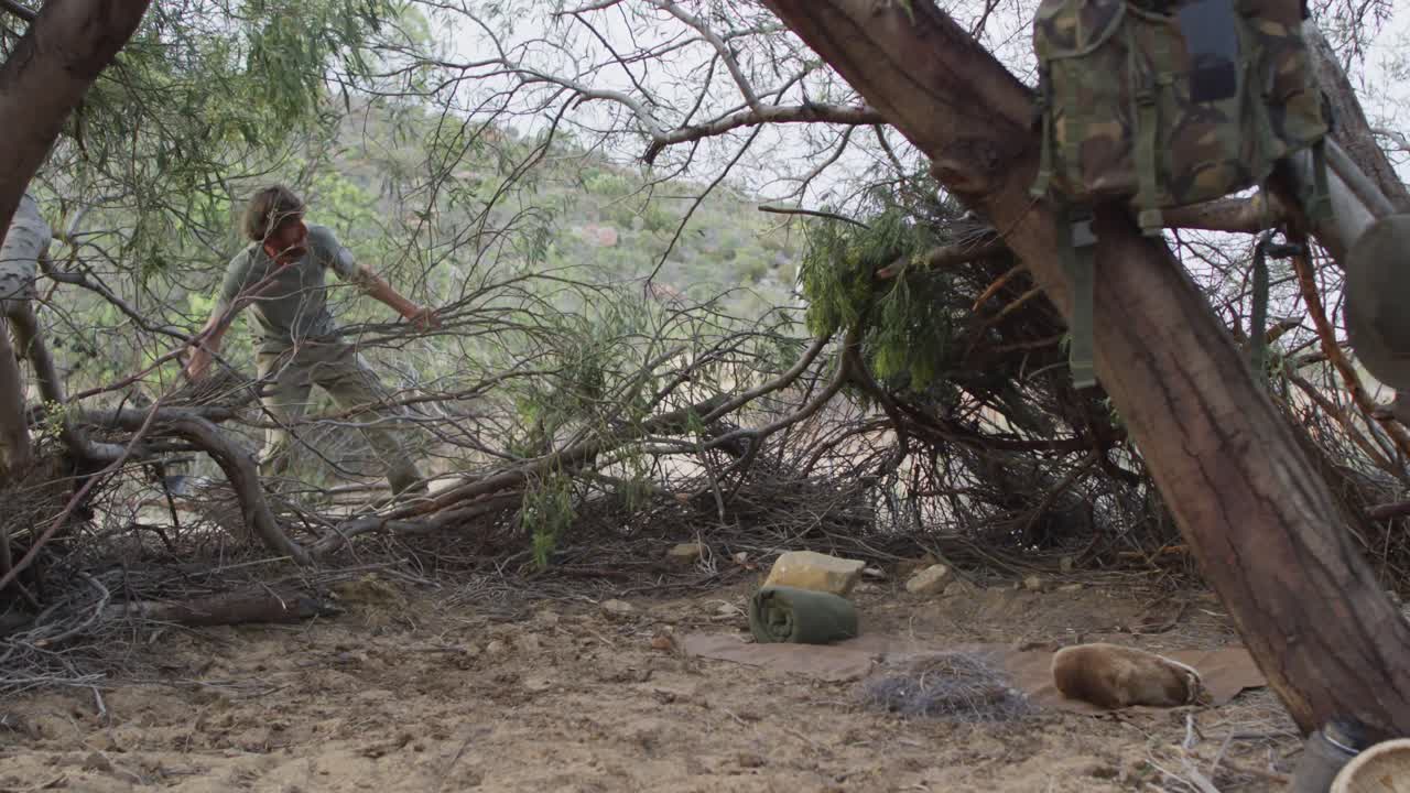 수염 이 있는 백인 남성 생존주의자 는 야생 에 있는 캠프 에서 피난처 를 마련 하기 위해 나무 가지 를 움직인다