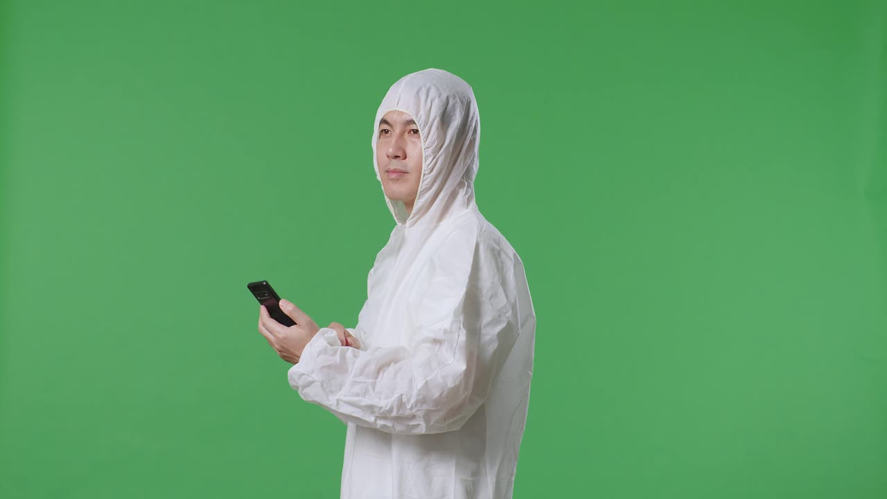 스마트폰을 사용하는 아시아 남성 과학자의 측면 뷰와 녹색 화면 배경에 서 있는 동안 주위를 둘러보십시오