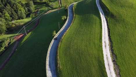 top down aerial - a vintage ural motorcycle rides along a narrow path between green fields, meadows, lawns