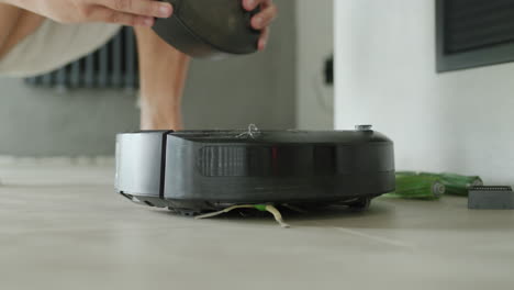 un hombre saca un cubo de basura de un robot aspirador
