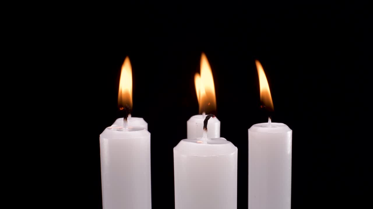 vista macro rotante candele bianche accese su sfondo nero, ricordo elegante o ricordo di filmati defunti