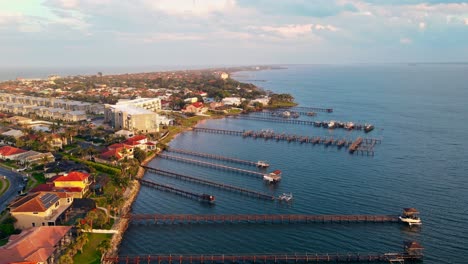 Una-Toma-Aérea-Alta-De-4k-De-Casas-Y-Edificios-Cerca-Del-Agua-Del-Océano-En-Melbourne,-Florida,-Con-Un-Muelle-Extendido-Hacia-El-Agua-Con-La-Puesta-De-Sol-Brillando-Cerca