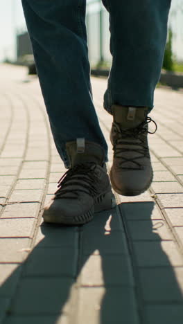 primer plano de piernas en movimiento, individuos caminando de cerca en un camino entrelazado con zapatillas de deporte y botas bajo la luz del sol brillante con fondo borroso con barandilla de hierro