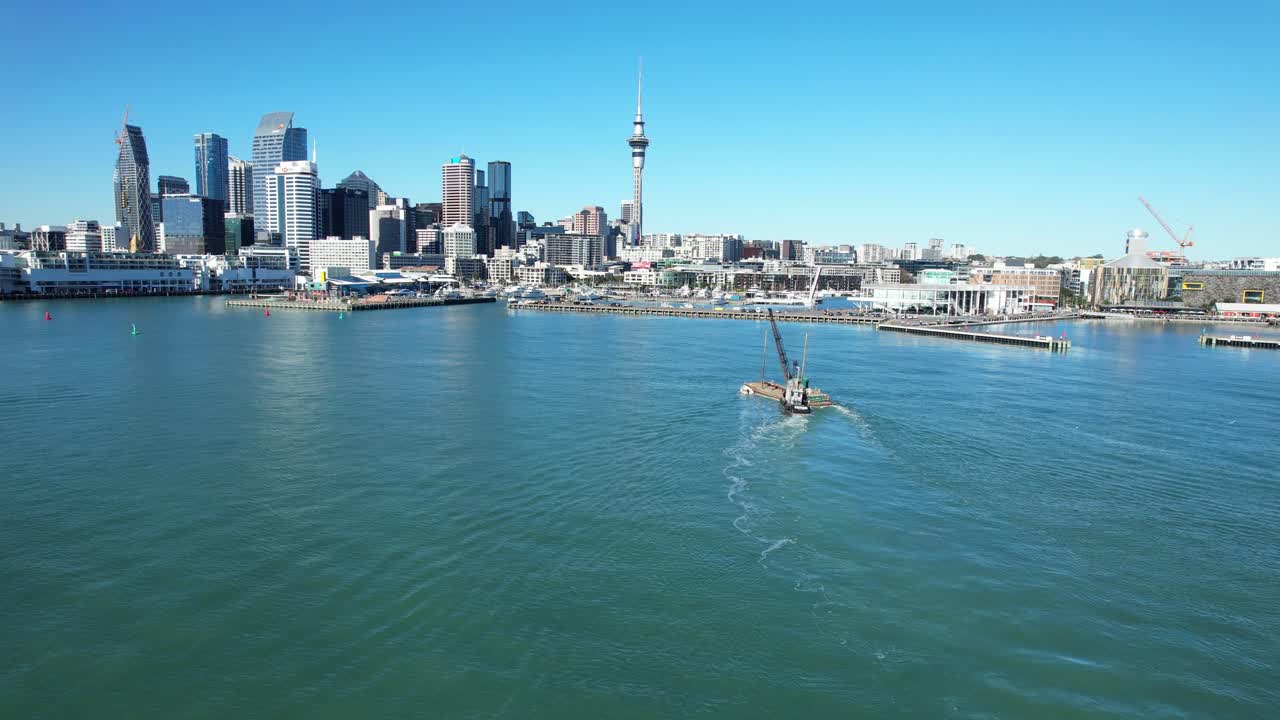 Auckland cityscape and harbor with a boat and crane on a clear day