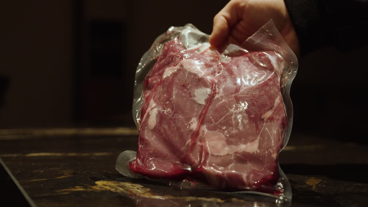 A hand holds a piece of vacuum-sealed meat, representing food preservation, extended shelf life, and hygiene in modern food storage