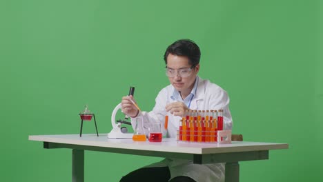 side view of asian man scientist sitting and making experiment with test tube on the table with microscope in the green screen background laboratory