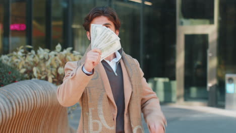 successful rich happy young indian man holding dollar bill money cash fan on downtown city street