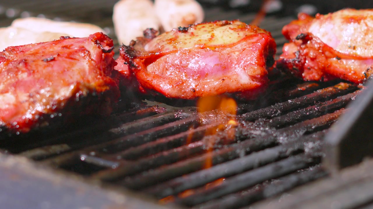 Cosce di pollo cinesi condite su barbecue caldo con fiamme in primo piano e luce solare intensa durante la stagione estiva