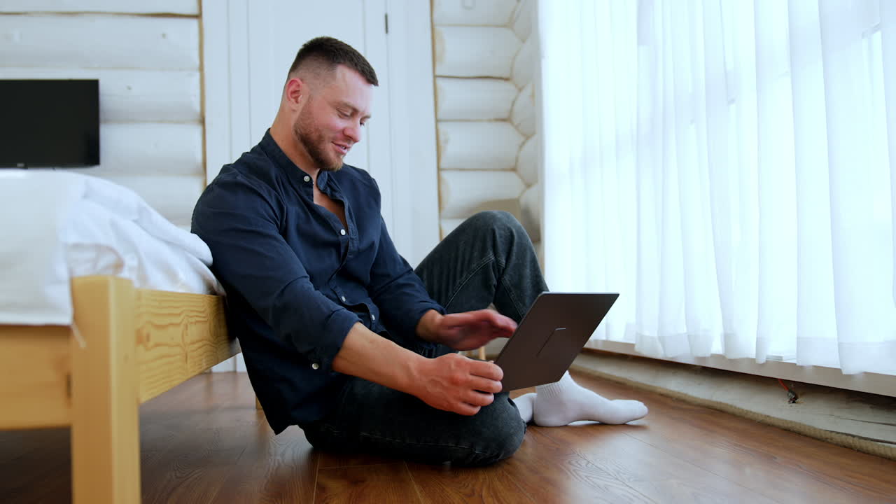 Happy smiling Caucasian man sitting on the floor uses his laptop. Online business concept.