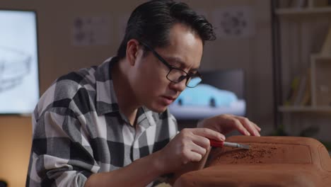 close up of asian man automotive designer having a headache while using rake or wire to smooth out the surface and create details in the sculpture of car clay in the studio