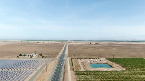 A-rising-shot-of-a-rural-road-surrounded-by-solar-panels-on-the-left-hand-side-and-vineyards-on-the-right