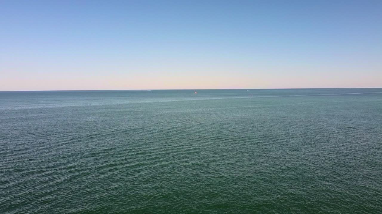 Aerial view over calm ocean with single small sailboat in vast seascape