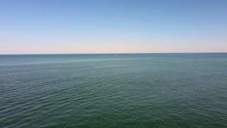 aerial view over calm ocean with single small sailboat in vast seascape