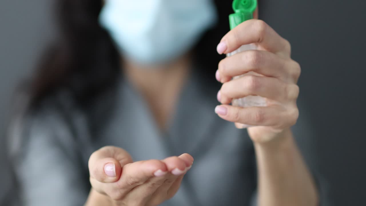 Woman applying hand sanitizer while wearing a medical mask