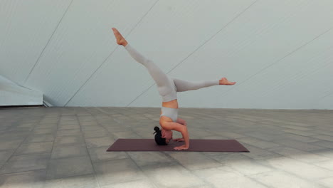 side view of brunette woman performing sirsasana ii yoga posture or headstand with variations of the posture