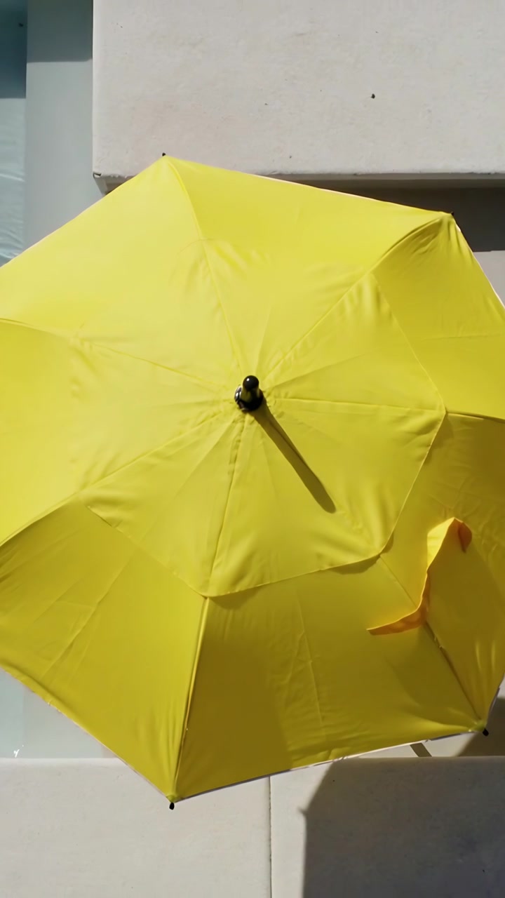 Video verticale: Riprese di un ombrello giallo che ondeggia nella brezza mentre la telecamera panoramica a bordo piscina mostra un nastro