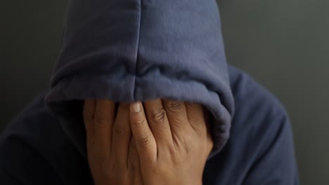 a man with his head down, hands covering his face. he is wearing a blue hooded sweatshirt.