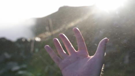 man touching waterdrops flying near waterfall