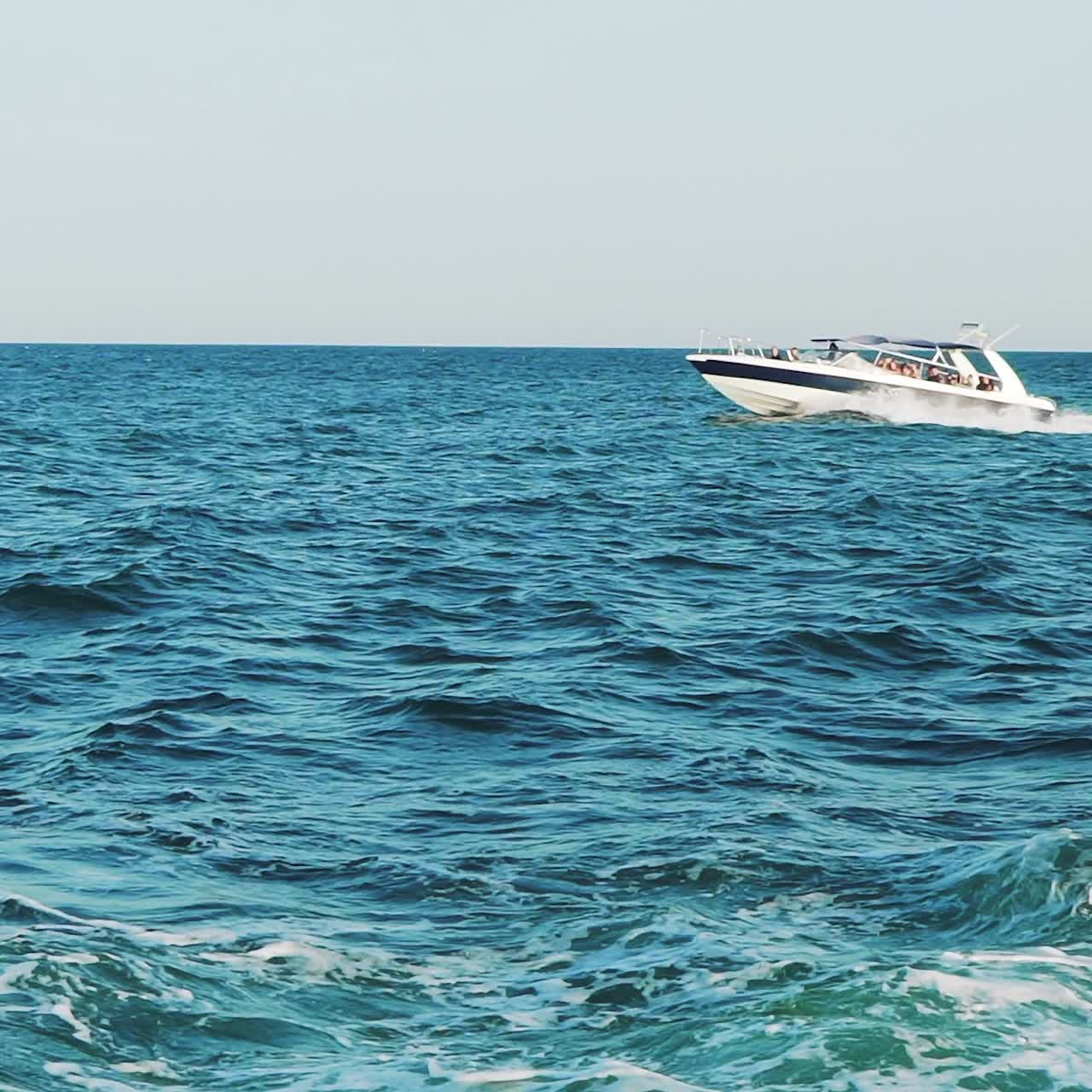 Boat with people is sailing on blue waves in the sea in the summer. Marine excursion. Slow motion. Seascape