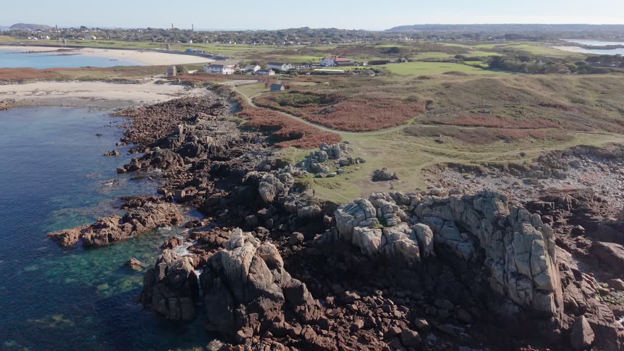 Lancresse Common Guernsey. Volo su brughiera e baie sabbiose con mari calmi e cristallini che mostrano la costa e le Torri Martello sotto il sole pomeridiano.