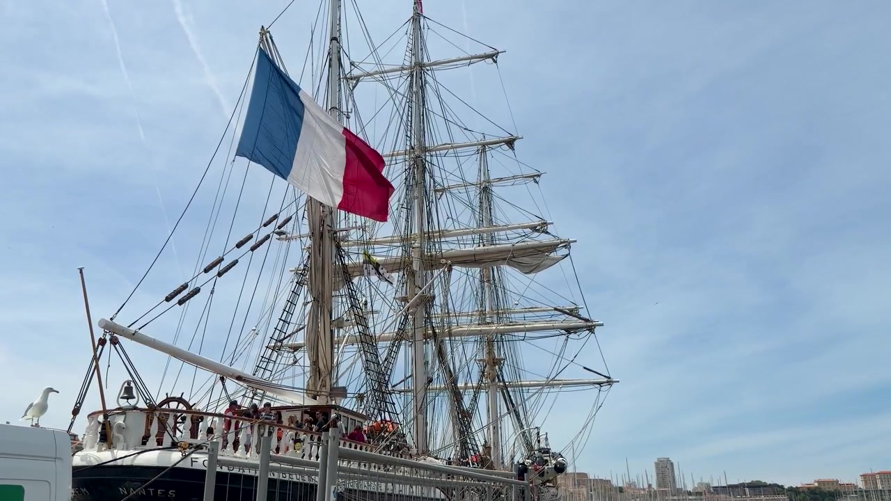 Et fransk flag vajer fra rigningen på et historisk sejlskib i Marseilles havn.