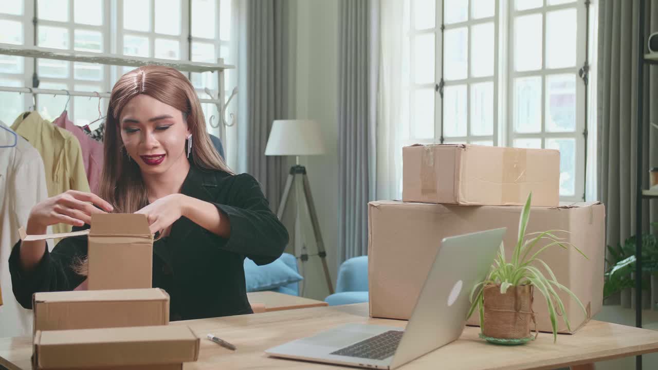 Young Asian Transgender Woman Business Owner With Boxes On The Table Happy Online Sales Job, Get An Order From Customers, Packing Box Delivery Products To Customers