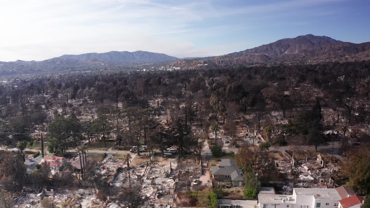 Aerial low dolly shot of the charred remains of homes and businesses destroyed in the Eaton Fire in Altadena, California. 4K