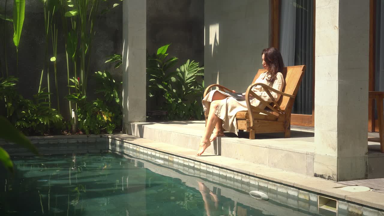 mujer expatriada trabajando en línea en su casa de lujo con piscina durante el día soleado y usando computadora portátil para trabajar desde casa temprano en la mañana, mujer profesional que usa tecnología haciendo trabajo remoto