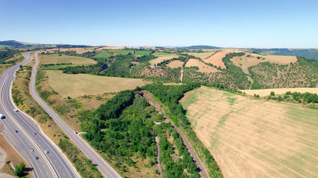 vista aérea de coches que conducen por la carretera a lo largo de los campos rurales y colinas en aveyron, francia