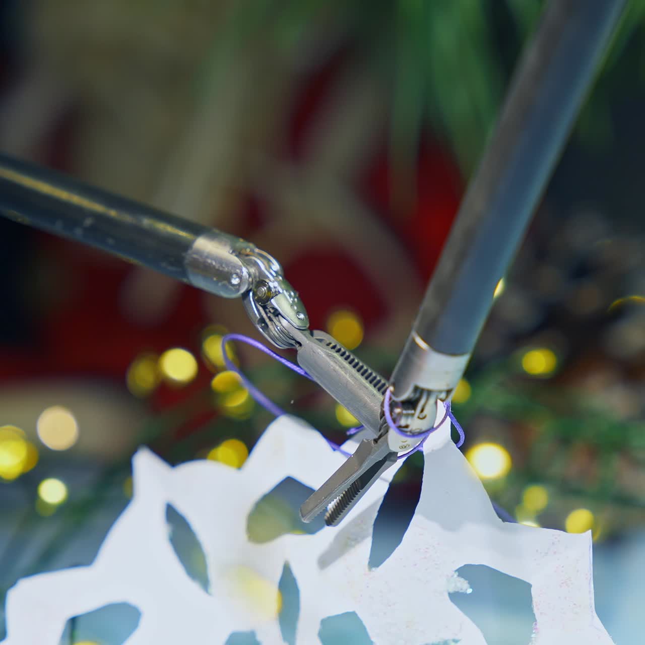 Tiny claws of the robotic arms tying the thread to the paper snowflake. Precise movements of the equipment. Christmas decorations at the backdrop