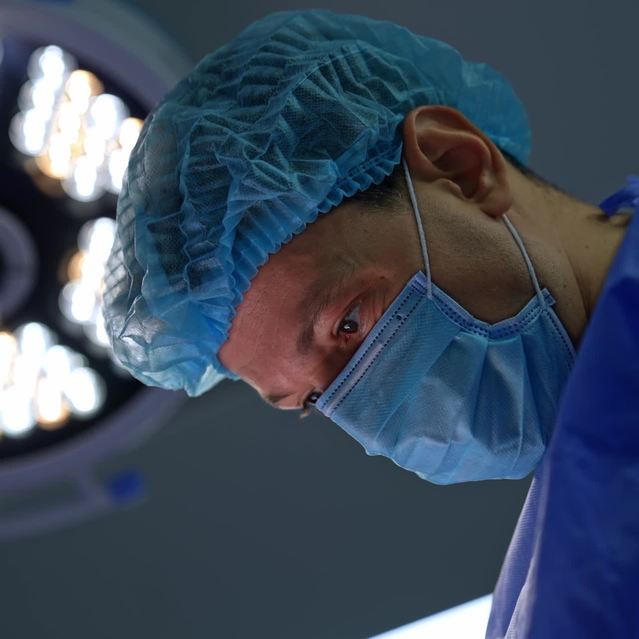 Intent look of a main surgeon at the operated area during operation. Portrait of a focused doctor performing surgery. Low angle view