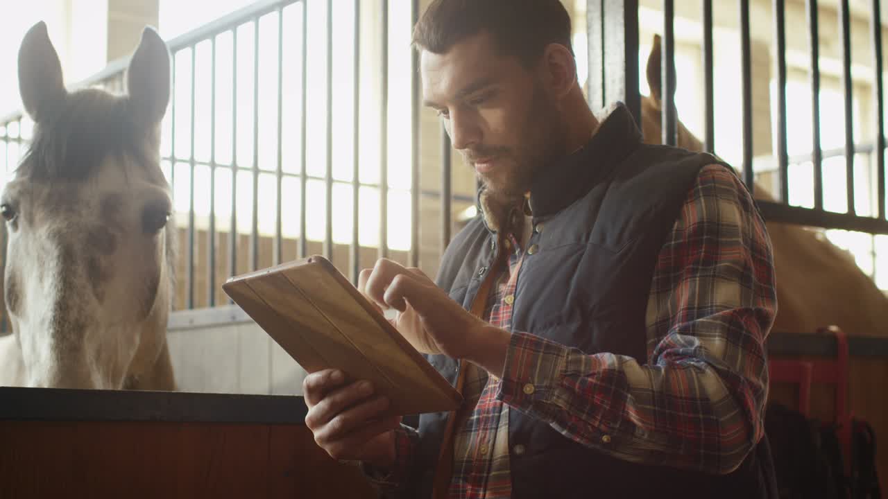 un hombre está usando una tableta junto a un caballo en un establo.