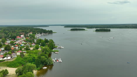aerial view of a lakeside town with boats, green trees, and waterfront homes - siemiany, jeziorak lake