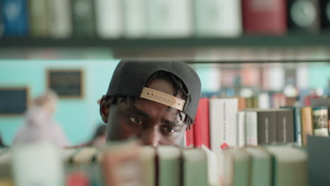 Primer plano en una biblioteca en el que se ve a un joven mirando entre las estanterías, escaneando una fila de libros, con las yemas de los dedos rozando los lomos mientras sus ojos siguen los títulos, en una búsqueda concentrada, con un fondo bokeh suave.