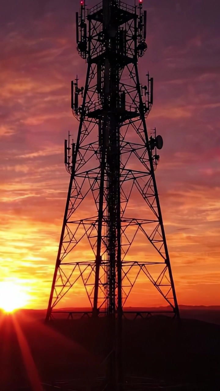 Splendida silhouette al tramonto di una torre di comunicazione illuminata da luci brillanti contro un cielo dai colori vivaci con sfumature di arancione, viola e blu.