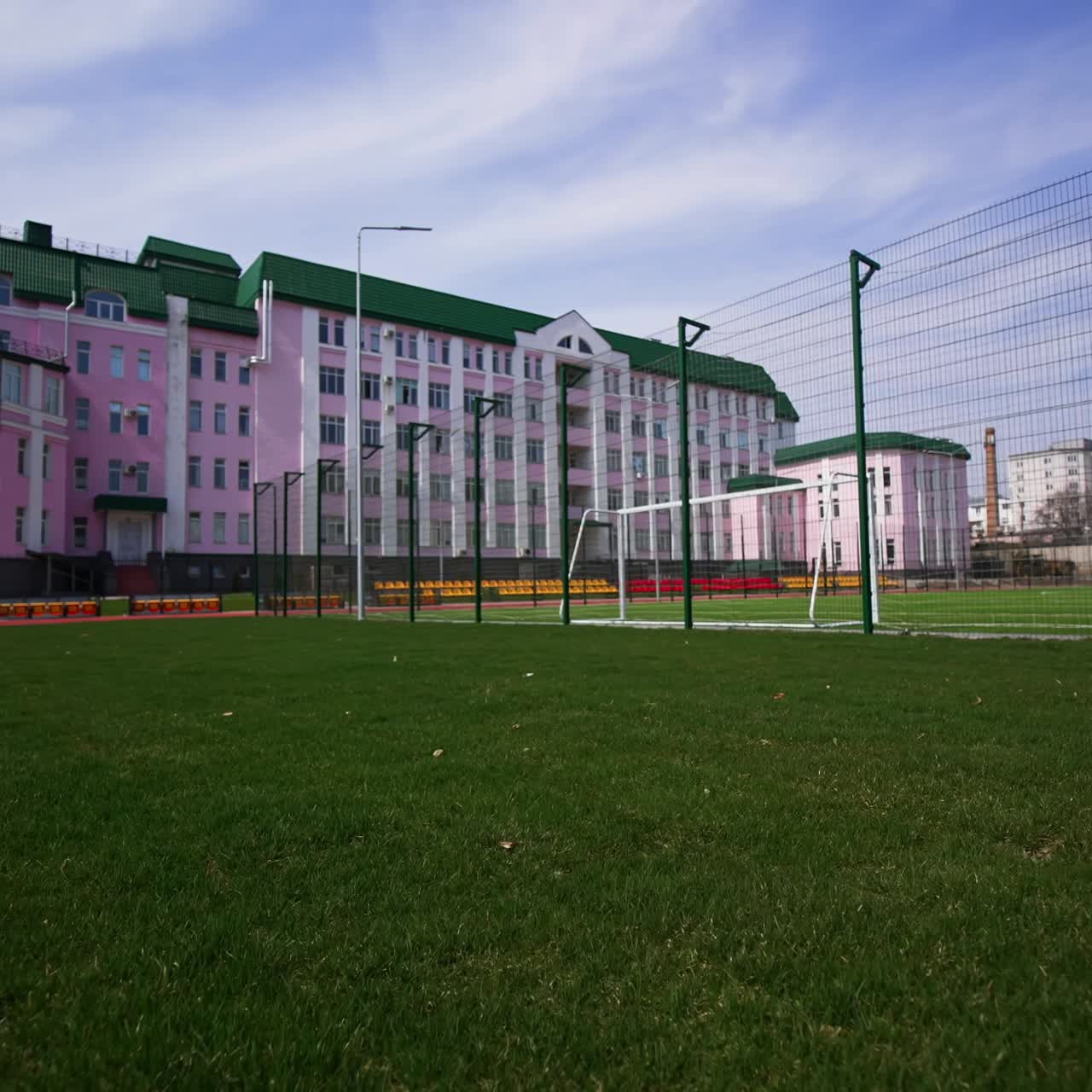 Red running track, green grass and football field located in front of the beautiful pink building. Low angle view. Blue sky at backdrop