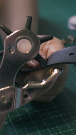 cu: professional girl tailor makes holes in stylish belt with punch pliers at green cushion board close view