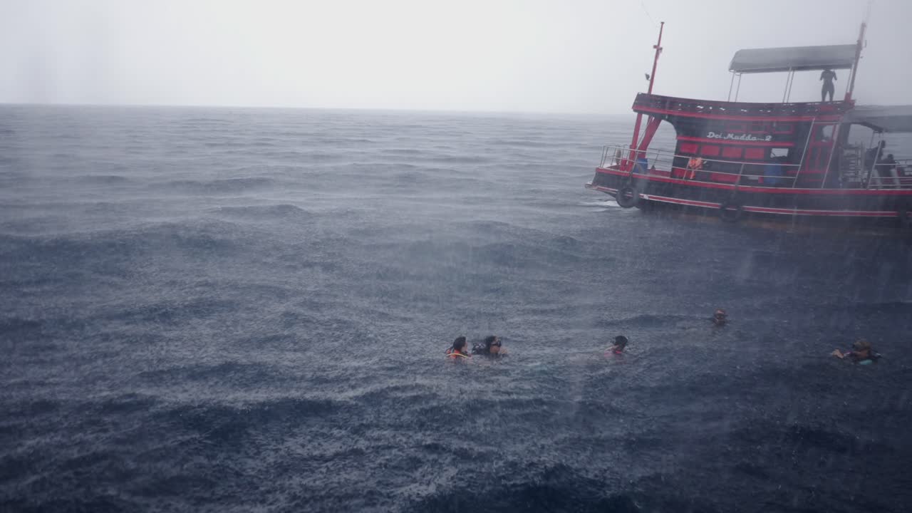 People swimming and snorkeling in the ocean during a heavy rain shower from a tour boat
