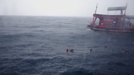 people swimming and snorkeling in the ocean during a heavy rain shower from a tour boat
