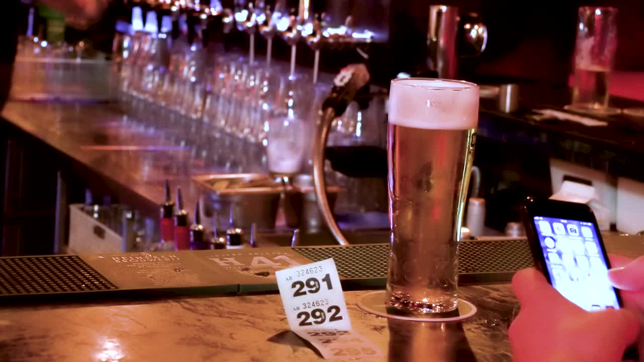 disfrutando de una pinta en un pub de dublín mientras envía mensajes de texto por teléfono y el barman trabaja detrás de la barra,