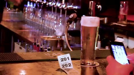 Enjoying-a-pint-in-a-Dublin-pub-while-texting-on-the-phone-and-bar-man-works-away-behind-the-bar,