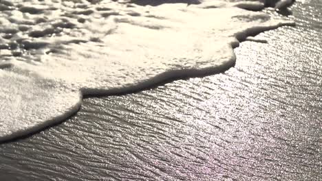 close-up camera follows wave crashing onto shore in slow motion on summer day