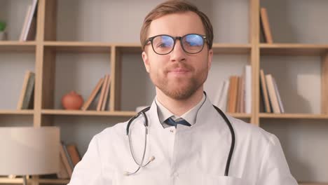 a young intern doctor in a white coat is looking at the camera and smiling.